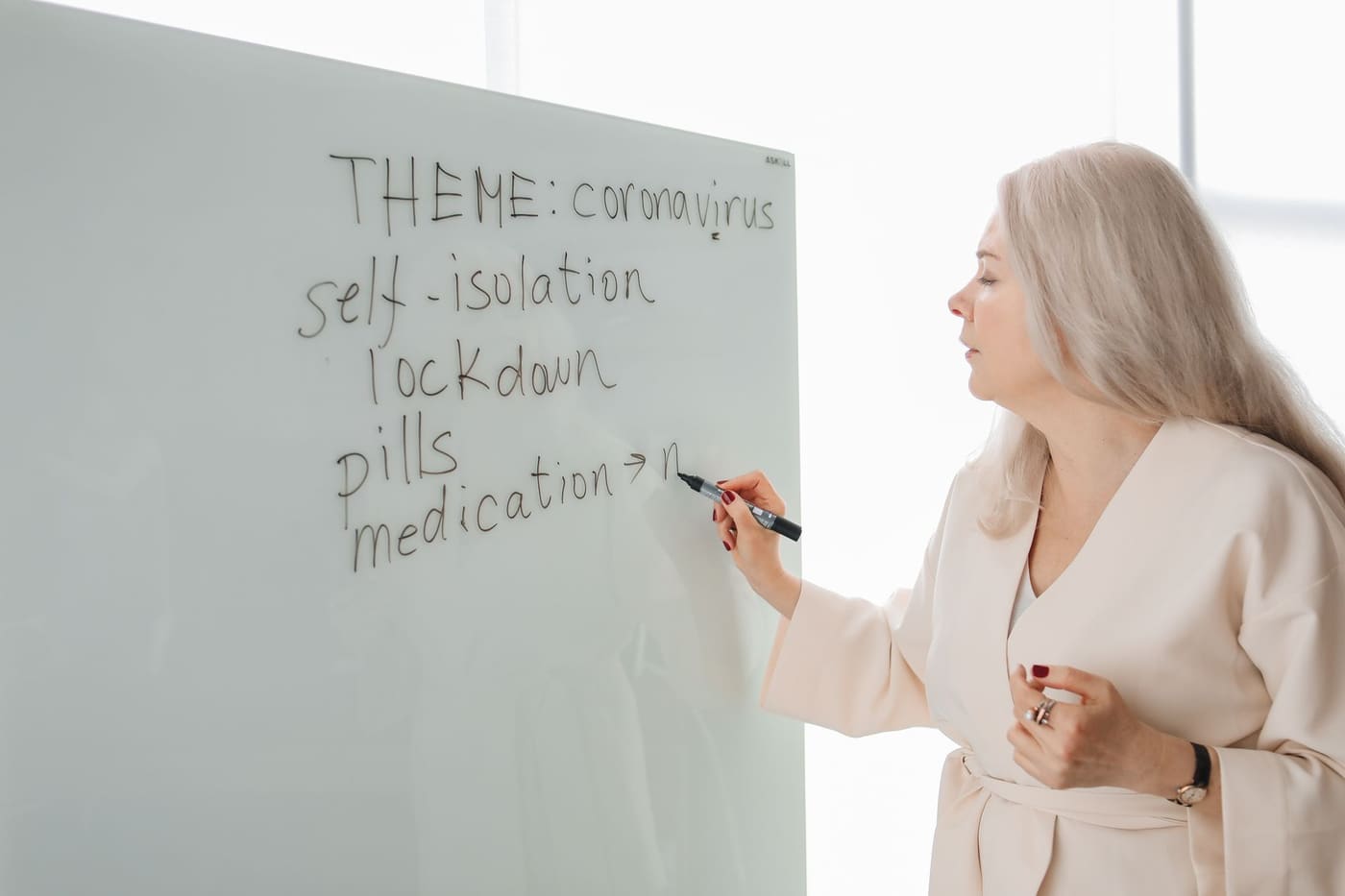 A health educator writing a lesson on coronavirus, self-isolation and medication on a whiteboard