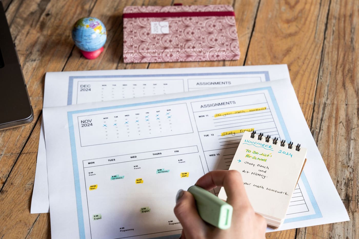 A hand with a marker plans a study schedule on a printed monthly calendar and to-do list