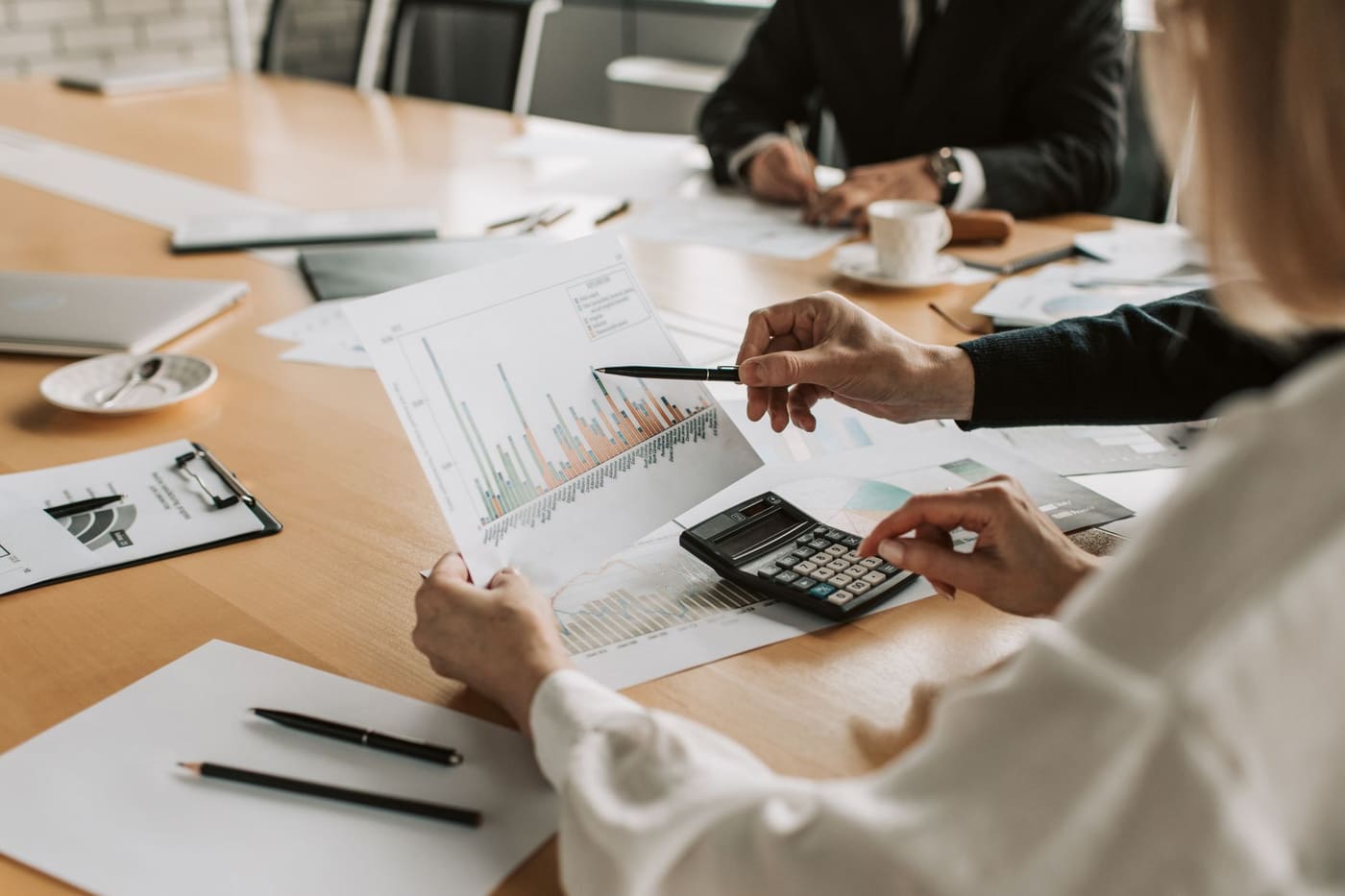 Colleagues at a conference table reviewing a bar chart with a pen and a calculator