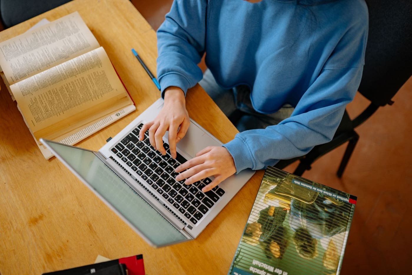 Overhead view of a student in a blue sweatshirt typing on a laptop beside open books