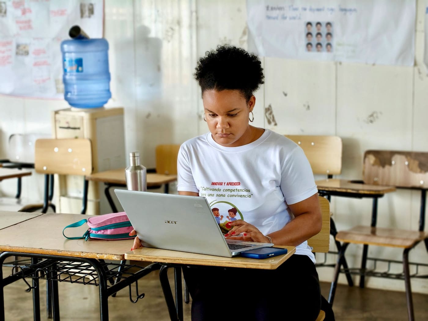 A graduate student works on a laptop at a desk in an empty classroom