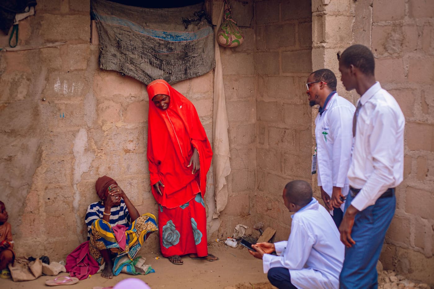 Health workers in white coats talk with women outside a home during a community health visit