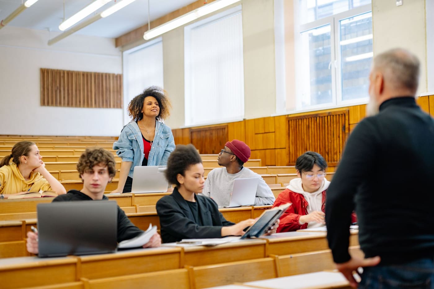 University students with laptops and notebooks in a tiered lecture hall listening to a professor