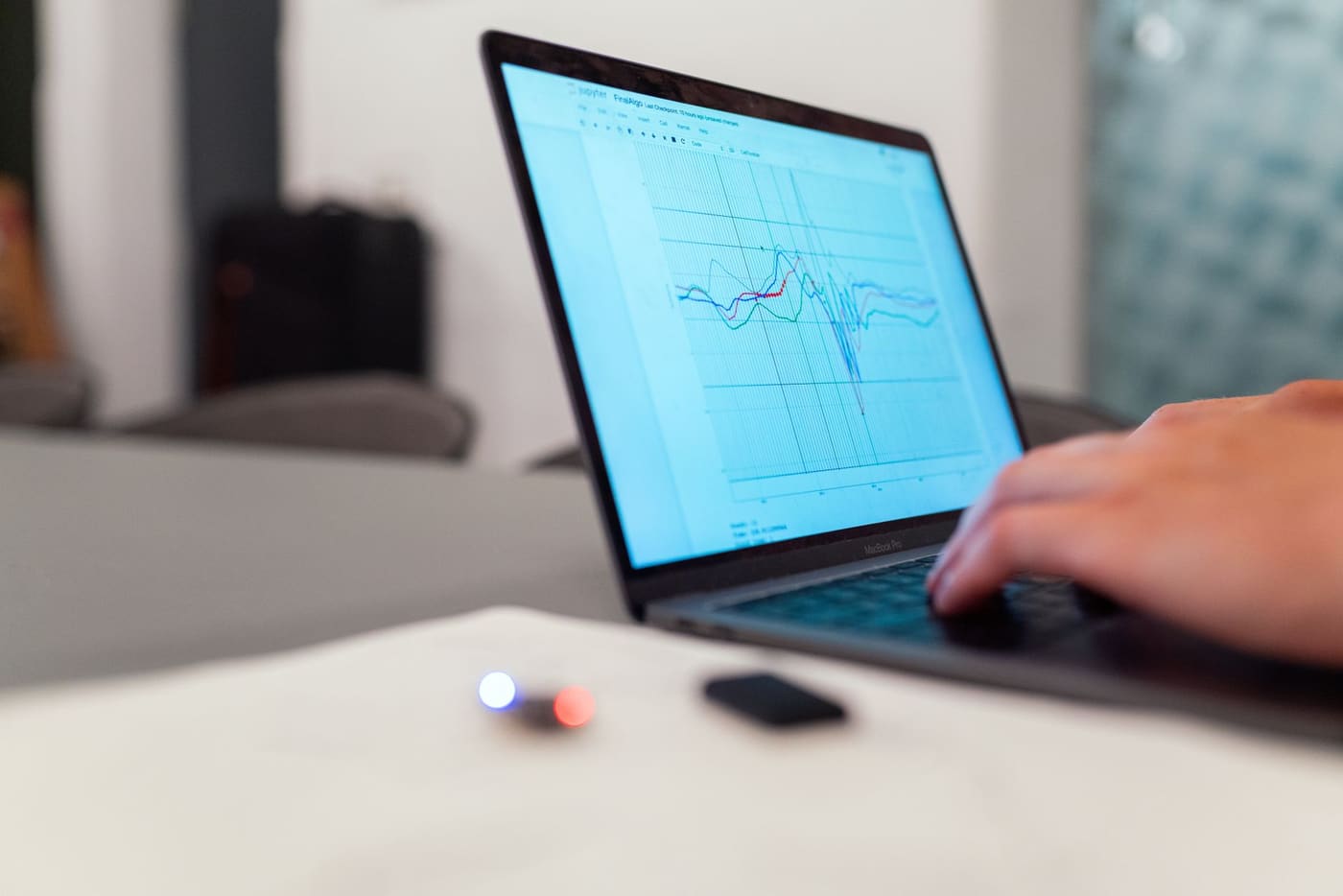 A hand on a laptop keyboard while the screen shows several line graphs in a data notebook
