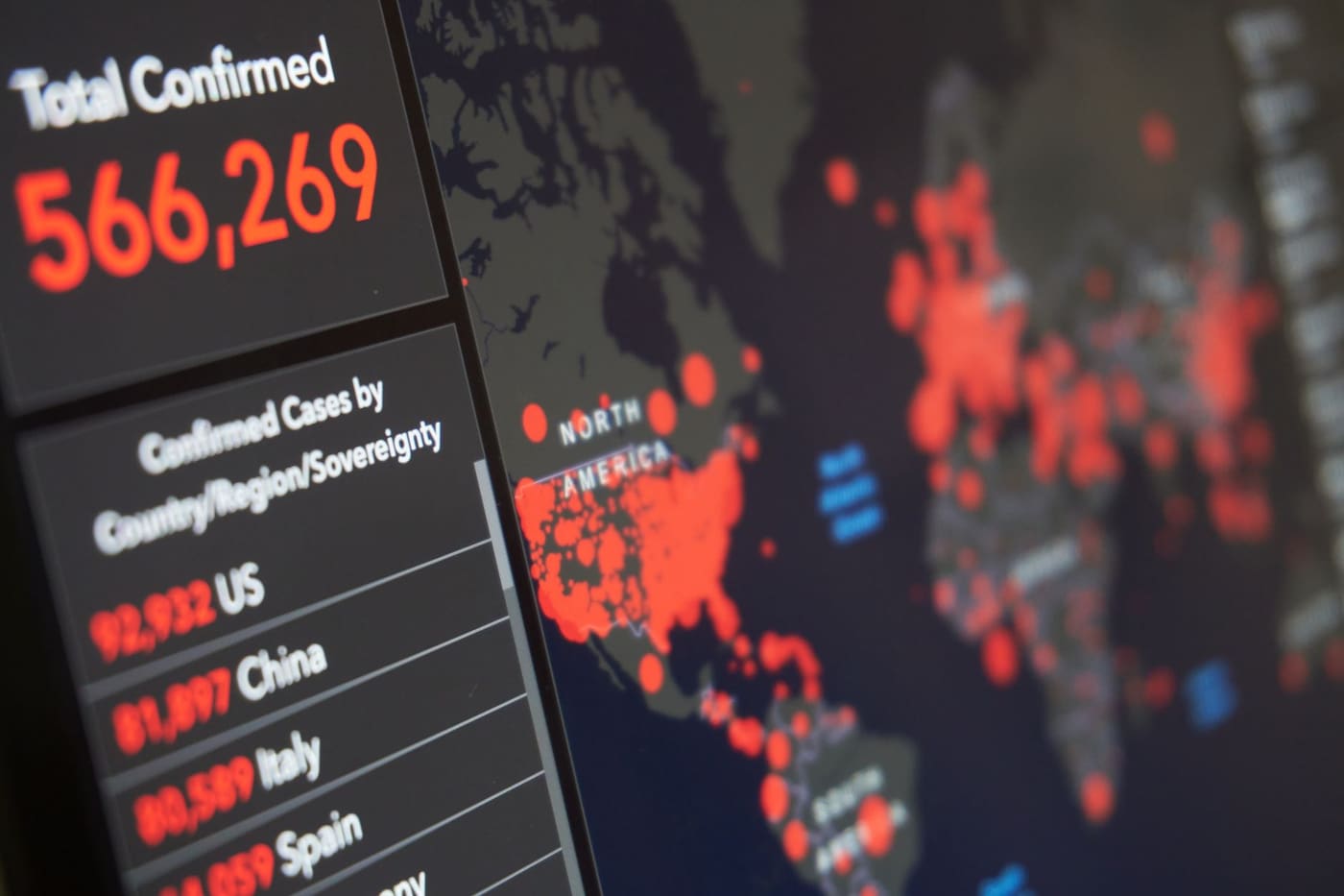 Close-up of a screen showing a world map with red circles marking confirmed disease cases and a table of case counts by country