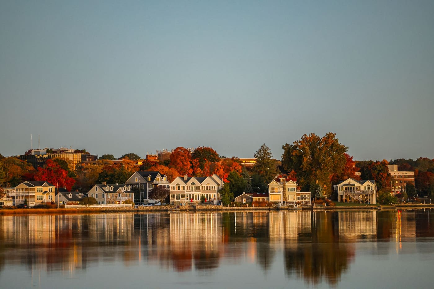 Waterfront houses in Stamford, Connecticut, reflected in still water among red and orange autumn trees at sunrise