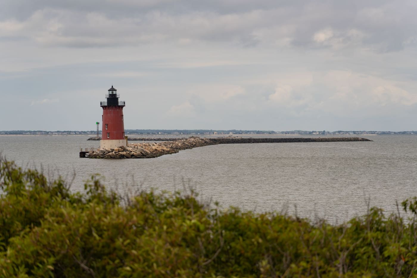 A red lighthouse at the end of a stone breakwater off Lewes, Delaware, under a cloudy sky
