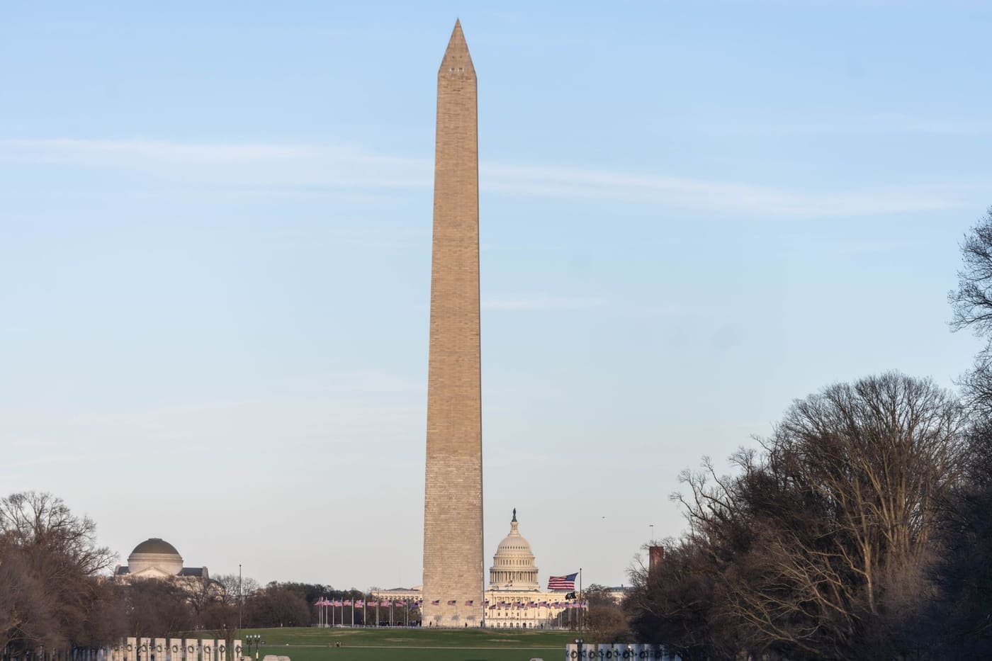 The Washington Monument on the National Mall with the U.S. Capitol dome and a ring of American flags behind it