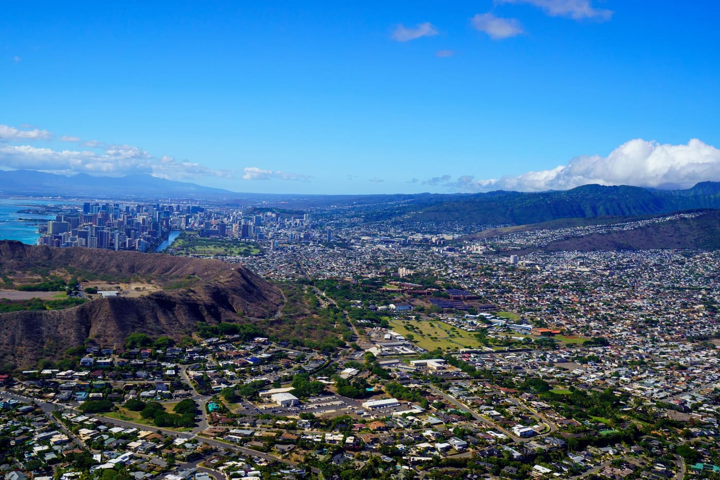 Aerial view of Honolulu from above Diamond Head crater, with Waikiki's towers along the coast and the Koolau mountains behind