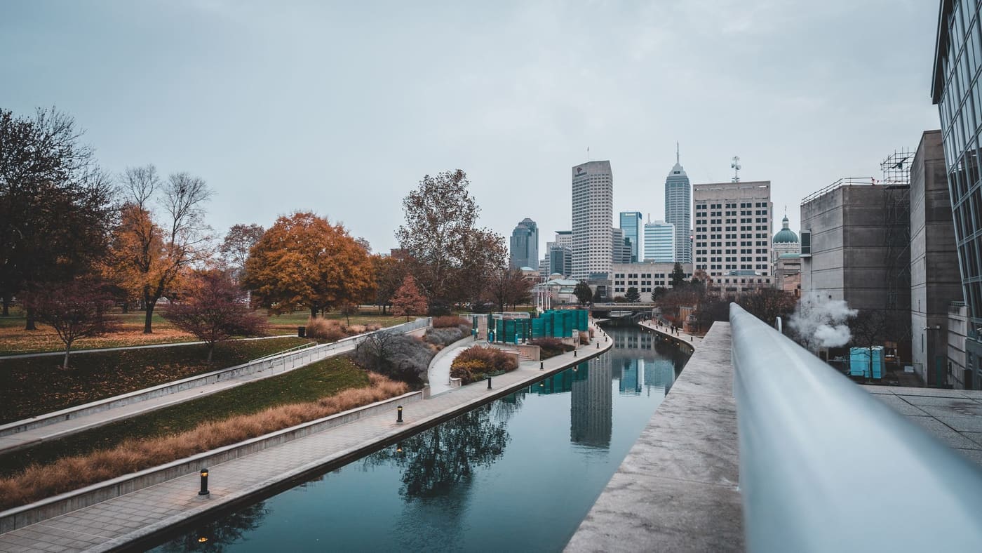 The downtown Indianapolis canal walk in autumn, with office towers and the Indiana Statehouse dome behind it
