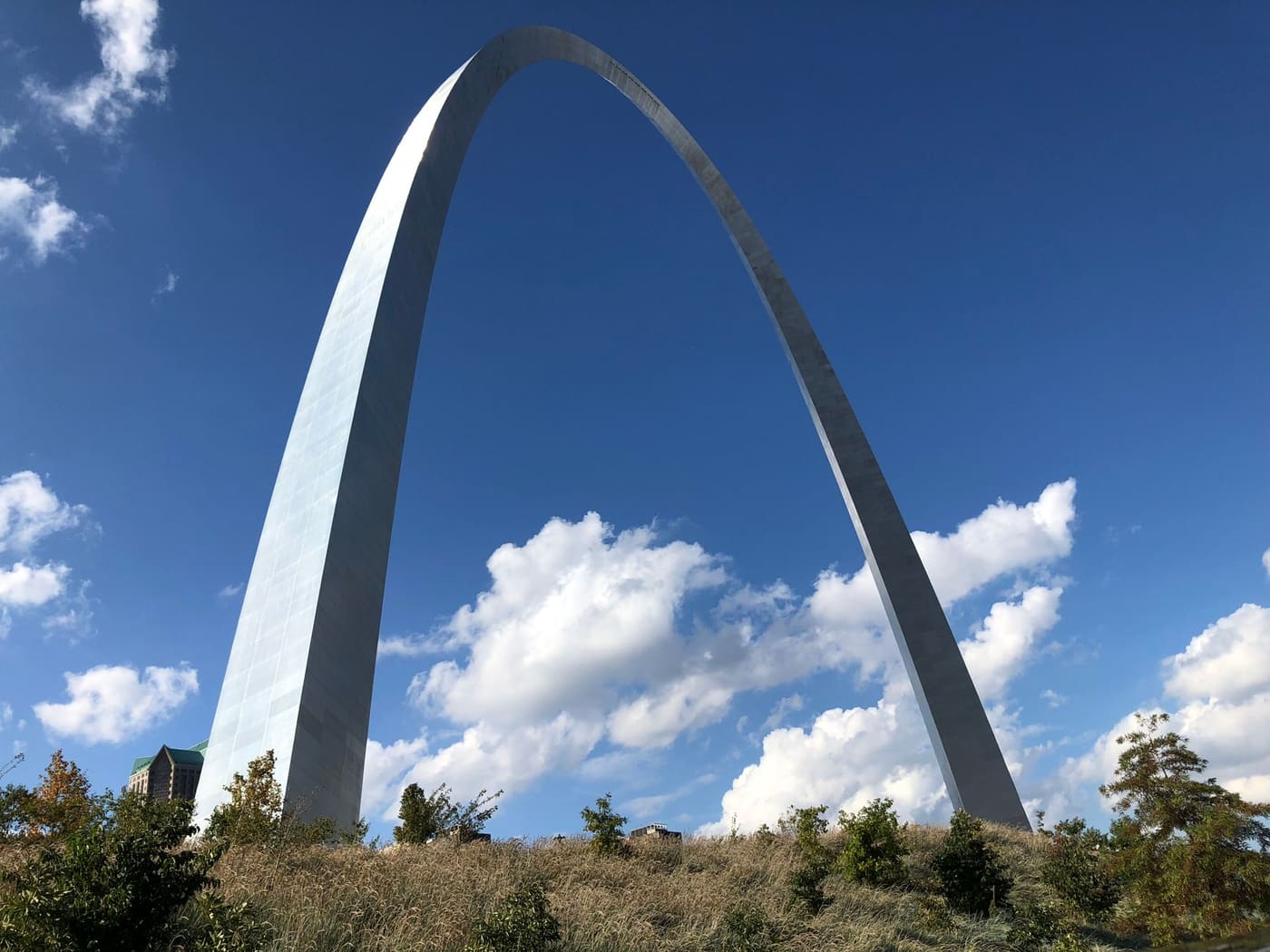 The stainless steel Gateway Arch in St. Louis rising above autumn grasses against a deep blue sky with white clouds