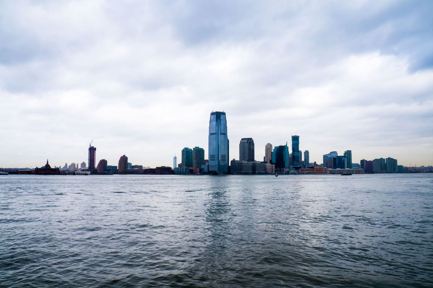 The Jersey City waterfront skyline seen across the Hudson River under a gray, cloudy sky