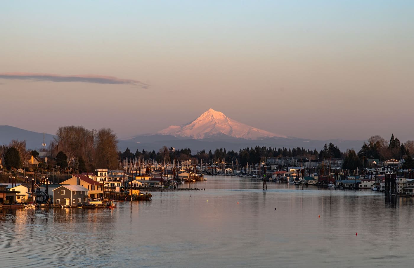 Snow-covered Mount Hood glowing pink at sunset above floating homes and a marina on a channel of the Columbia River in Portland