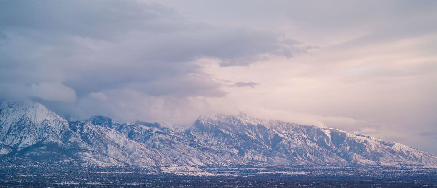 Snow-covered Wasatch Range under low clouds above the Salt Lake Valley at dusk